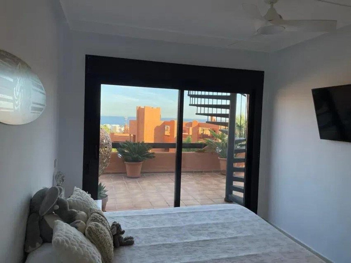 Bedroom with a sliding door leading to a terrace offering a view of the sea and orange buildings.