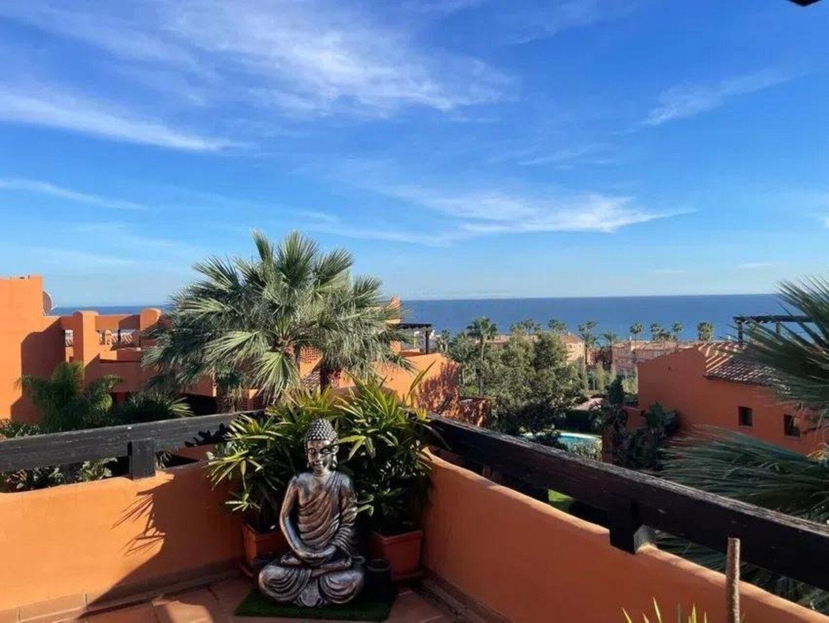 Terrace with sea view, palm trees, and a Buddha statue in front of potted plants.