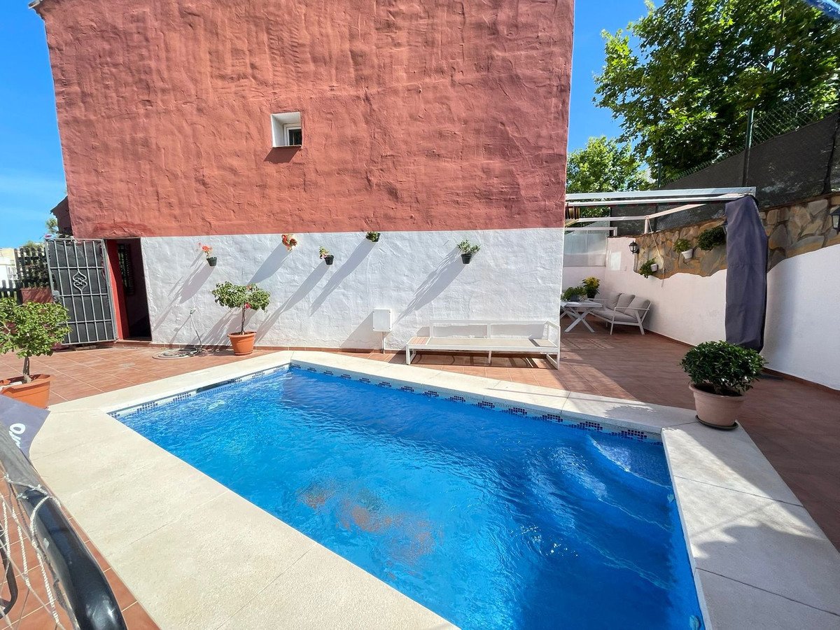 Backyard pool with blue water, white tiled deck, red and white walls, and potted plants under sunny sky.