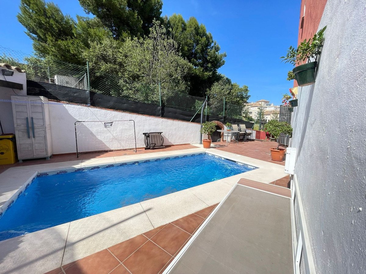 Backyard with swimming pool, patio, and greenery under a clear blue sky.