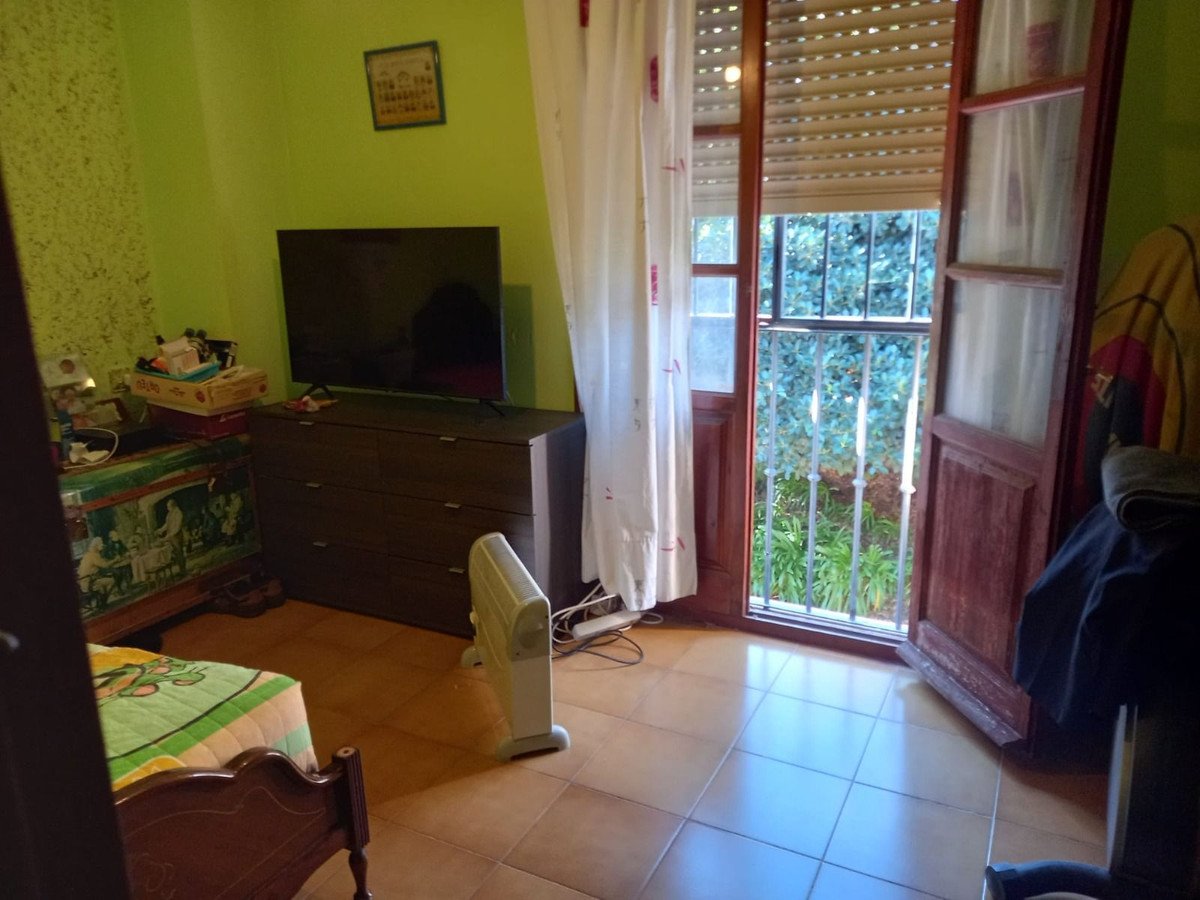 Bedroom with a double bed, dresser, television, and a balcony door with green garden view.