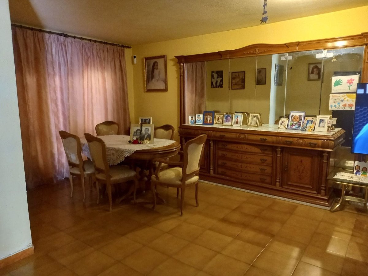 A formal dining room with a round table and chairs, featuring a large antique mirror cabinet displaying family photos.