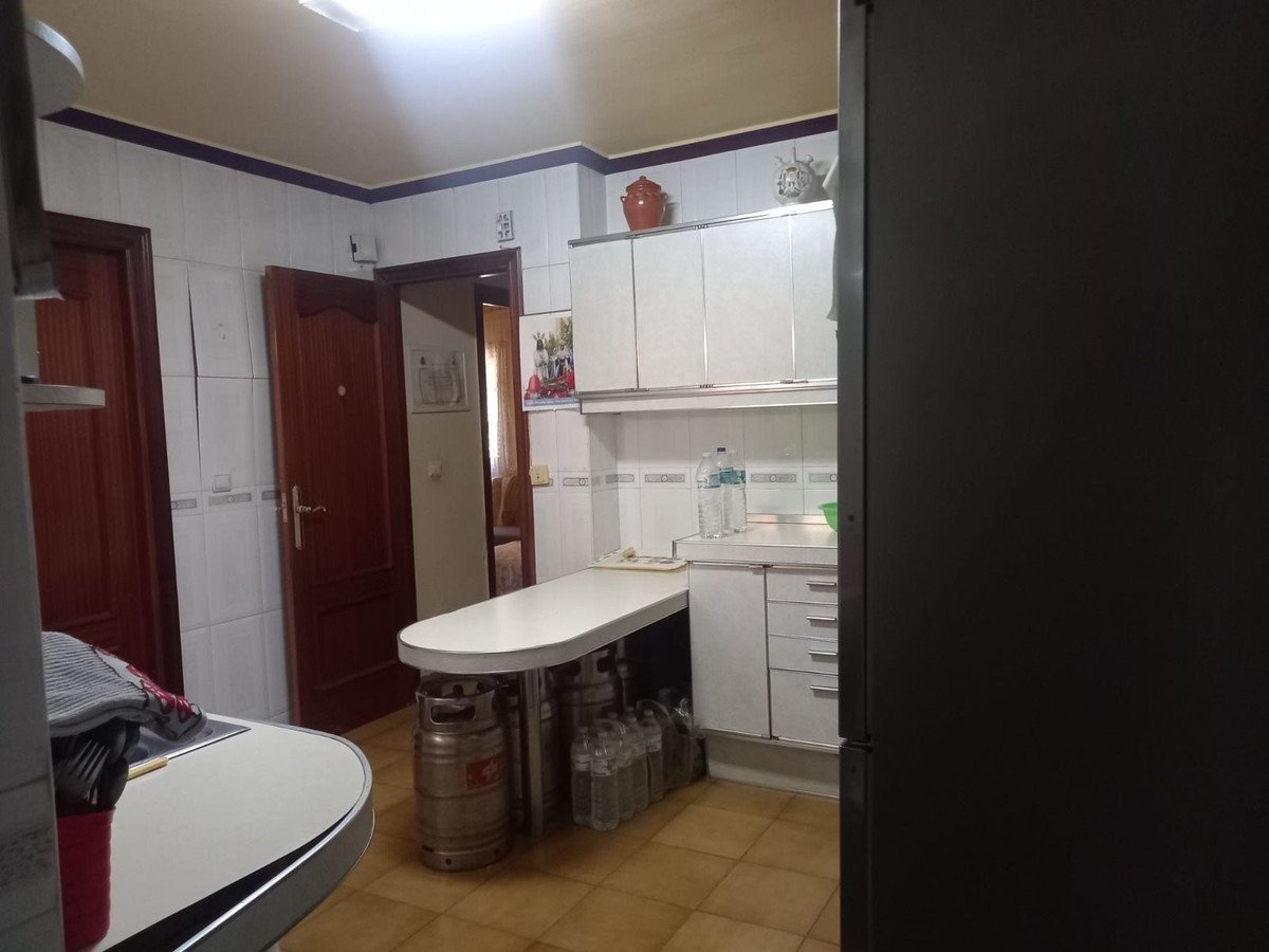 A kitchen featuring white cabinets, a curved countertop, and wooden doors. Water bottles and kegs are visible.