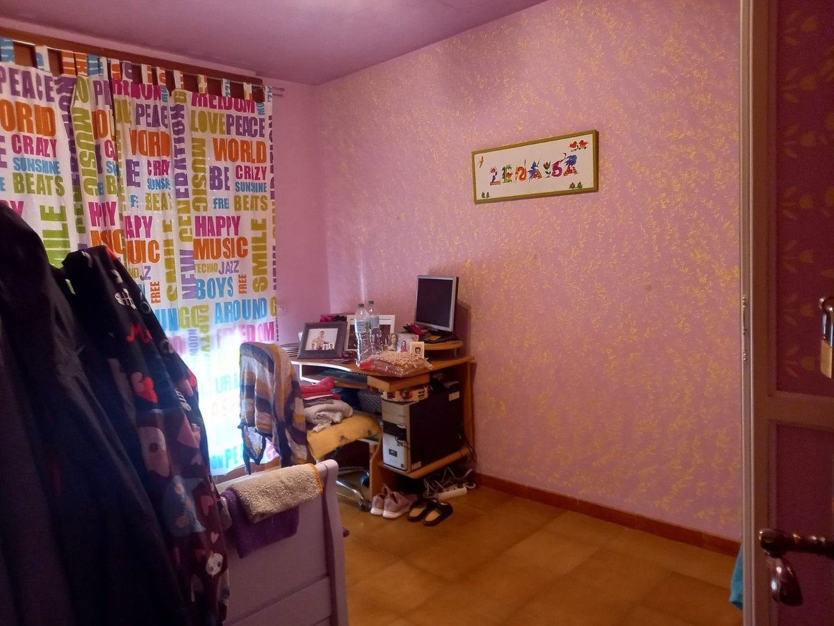 A pink bedroom with colorful patterned curtains, a desk with a computer, and artwork on the wall.
