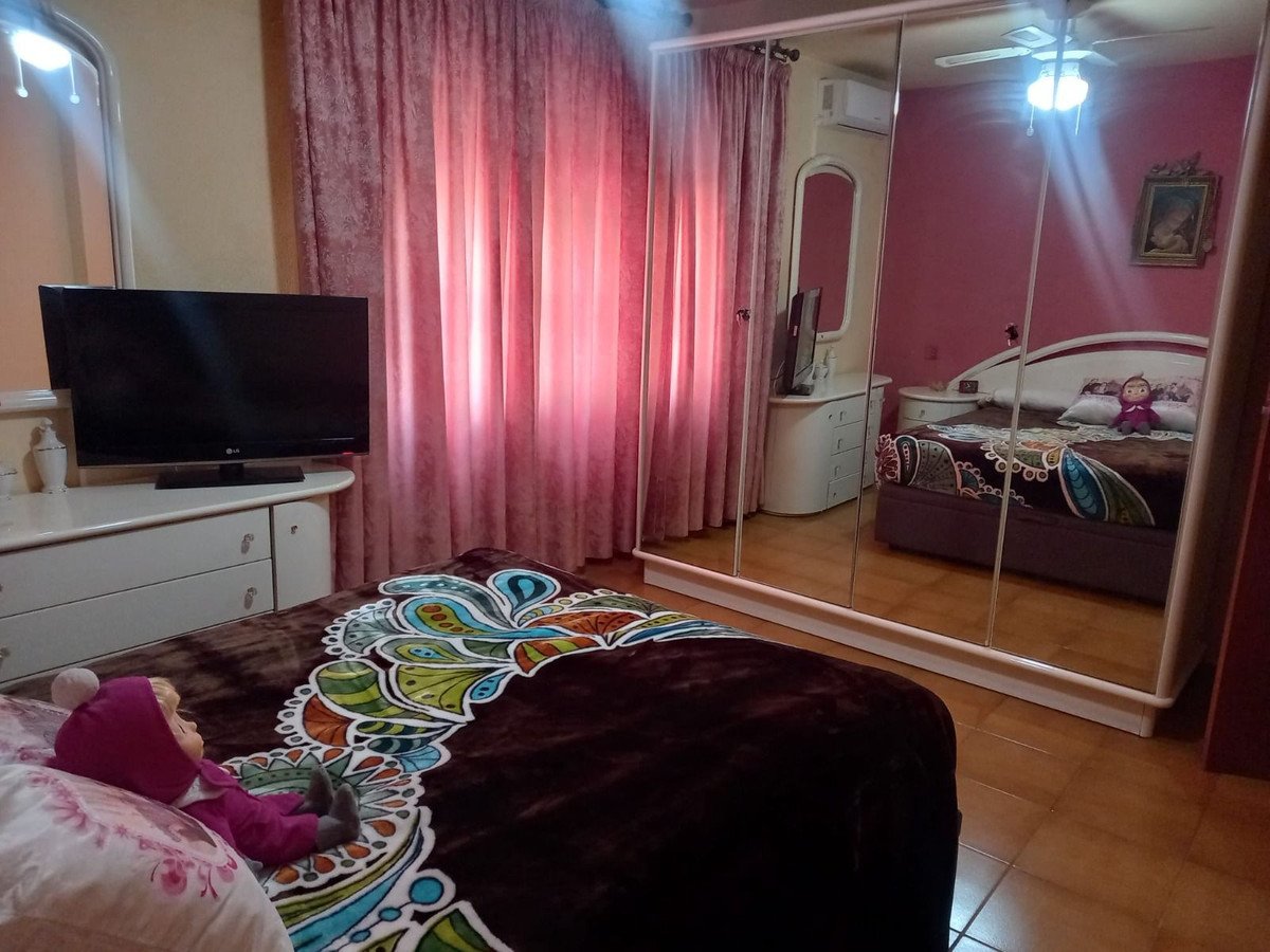 A bedroom featuring a large TV, a dresser, a bed with decorative pillows, and mirrored wardrobe doors reflecting the room.