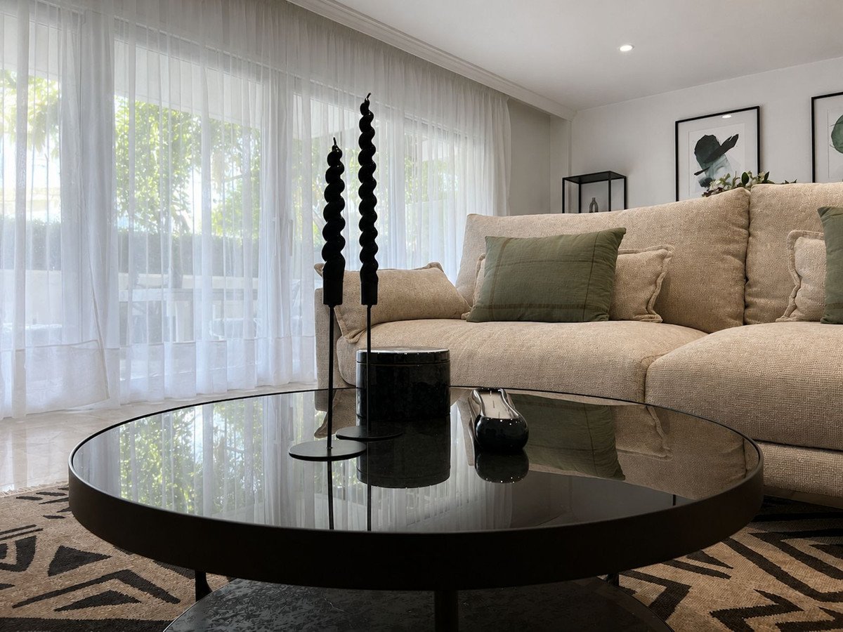 Modern living room with a beige sectional sofa, decorative candles on a black coffee table, and sheer curtains with outdoor views.