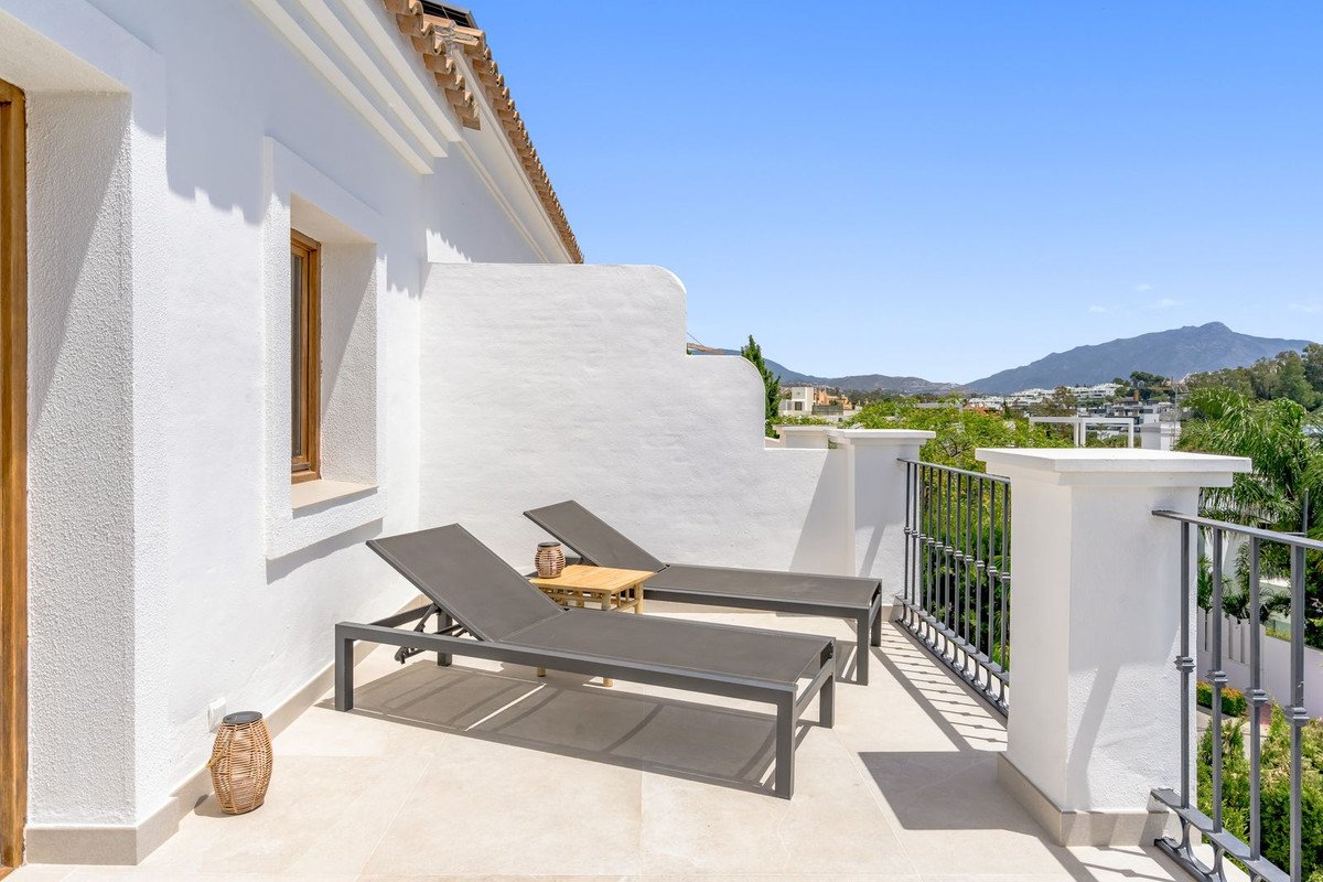 Sunlit balcony with two lounge chairs, white walls, and mountain views.
