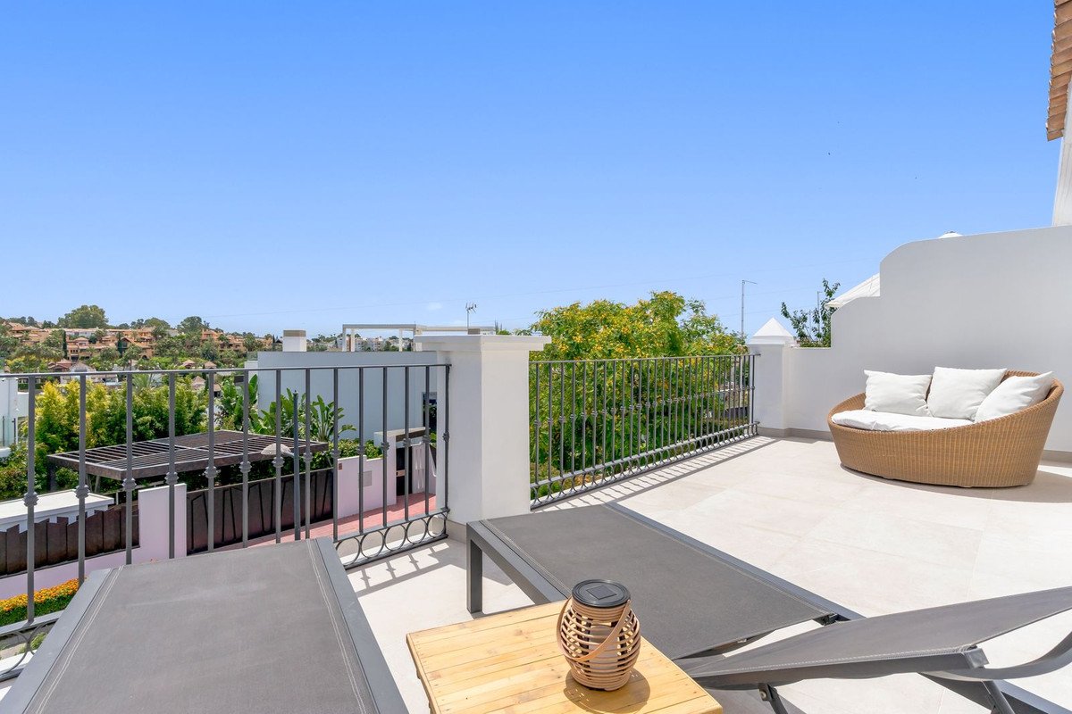 Rooftop terrace with lounge chairs, wicker sofa, and panoramic view of greenery and buildings under a clear blue sky.