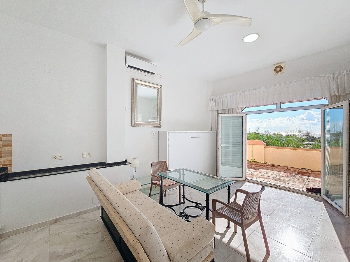 Living area with sofa, glass table, and chairs, opening onto a terrace with a distant sea view.