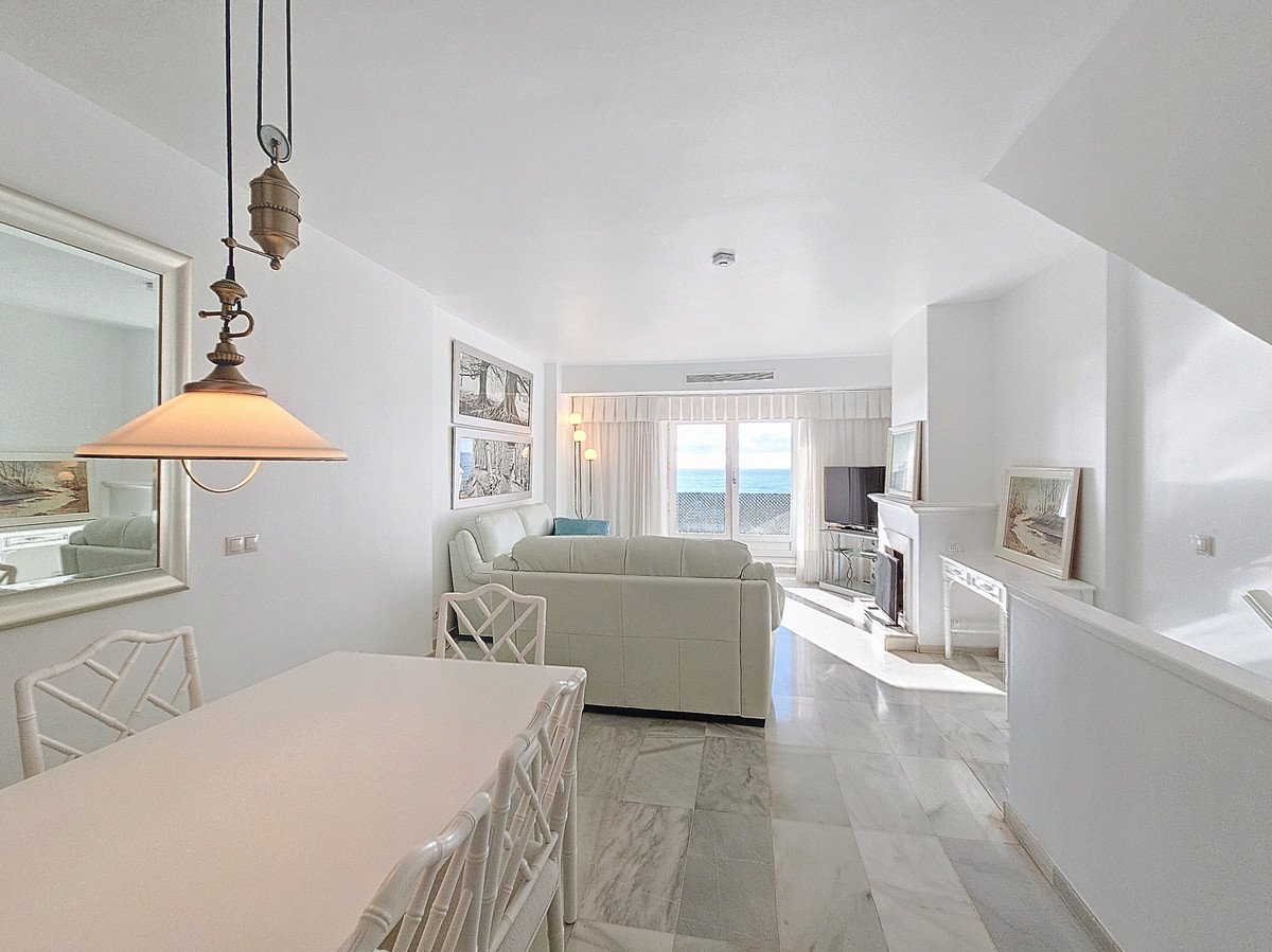 Spacious white living room with leather sofas, fireplace, and large windows offering a beautiful sea view.