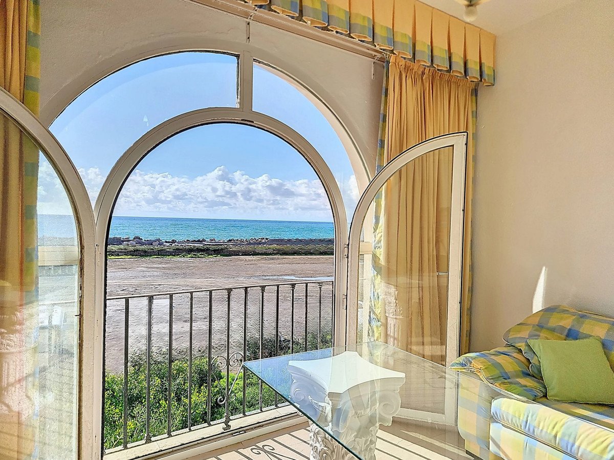View of the sea through an arched window and balcony doors, with a sofa and coffee table inside.