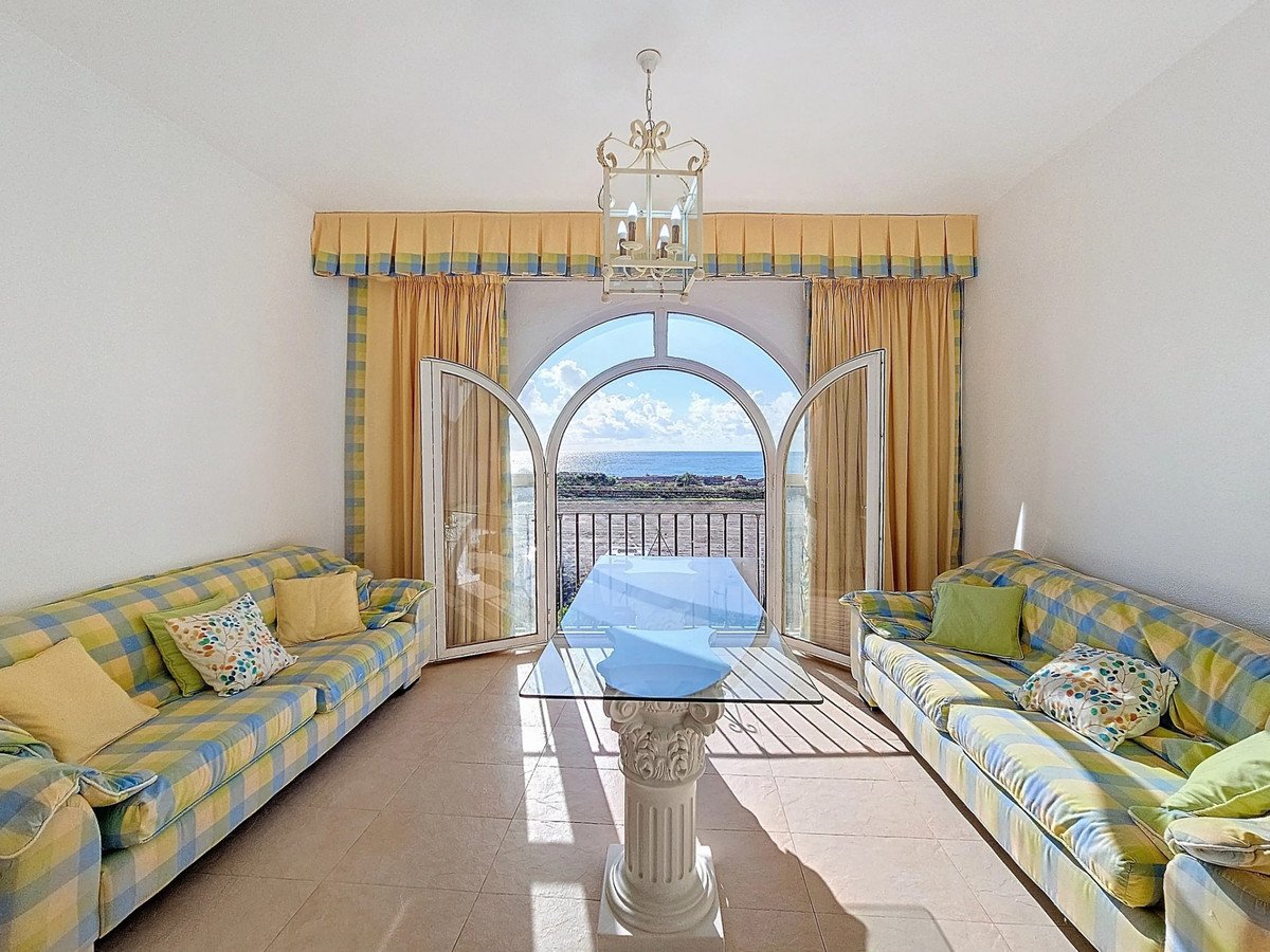 A bright living room with two checkered sofas, a glass table, and arched doors opening to a beautiful sea view.