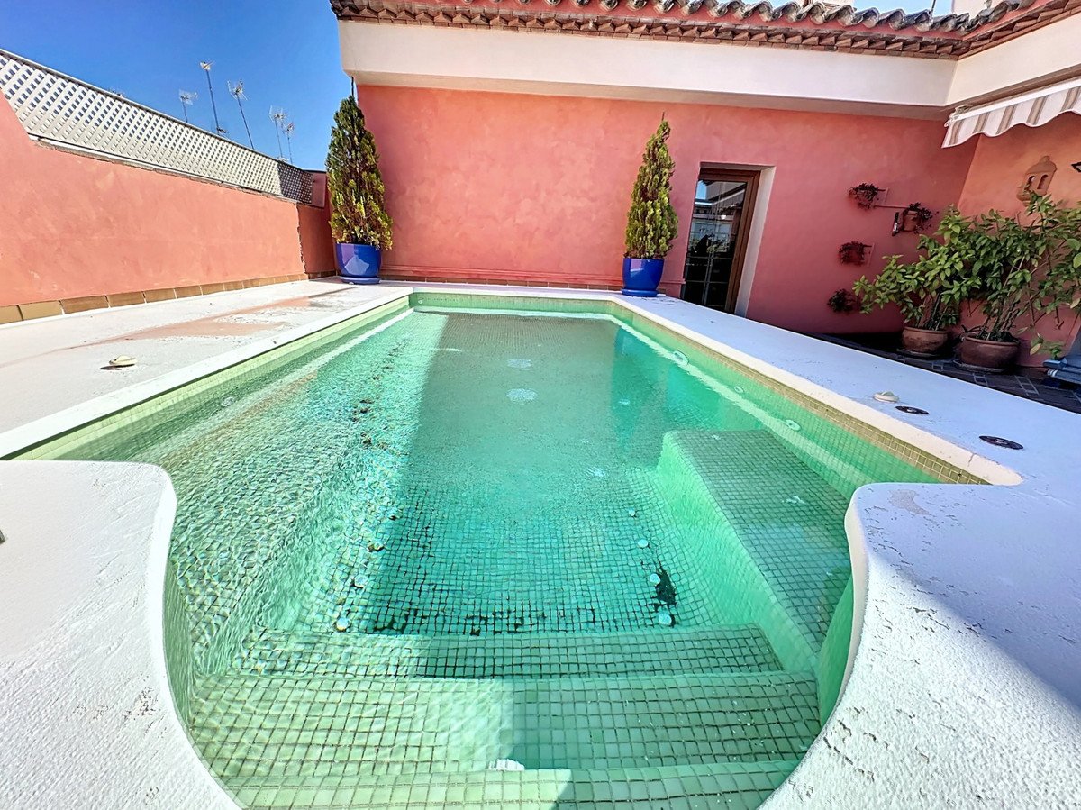 Swimming pool in tiled patio with pink walls and potted plants