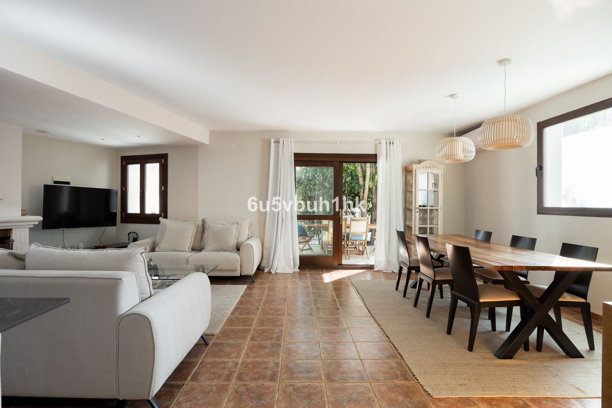 Spacious living and dining room with comfortable sofas, large wooden table, and sliding glass doors leading to an outdoor patio area.