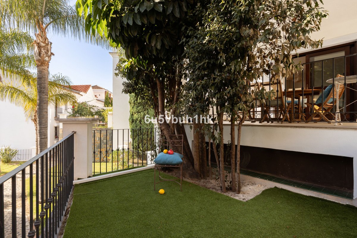 Artificial grass garden area with a chair and fruit, leading to a balcony with outdoor seating and trees.