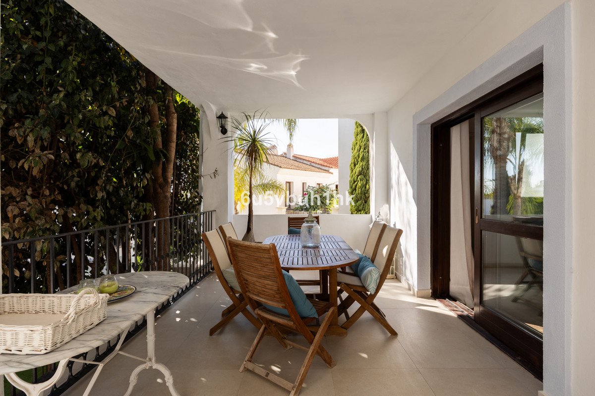 Covered terrace with wooden dining table and chairs, offering a view of rooftops and greenery.