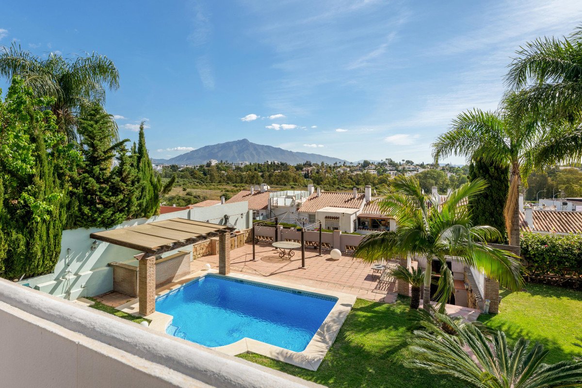 A private swimming pool and patio area with a distant mountain view, surrounded by lush greenery and palm trees.
