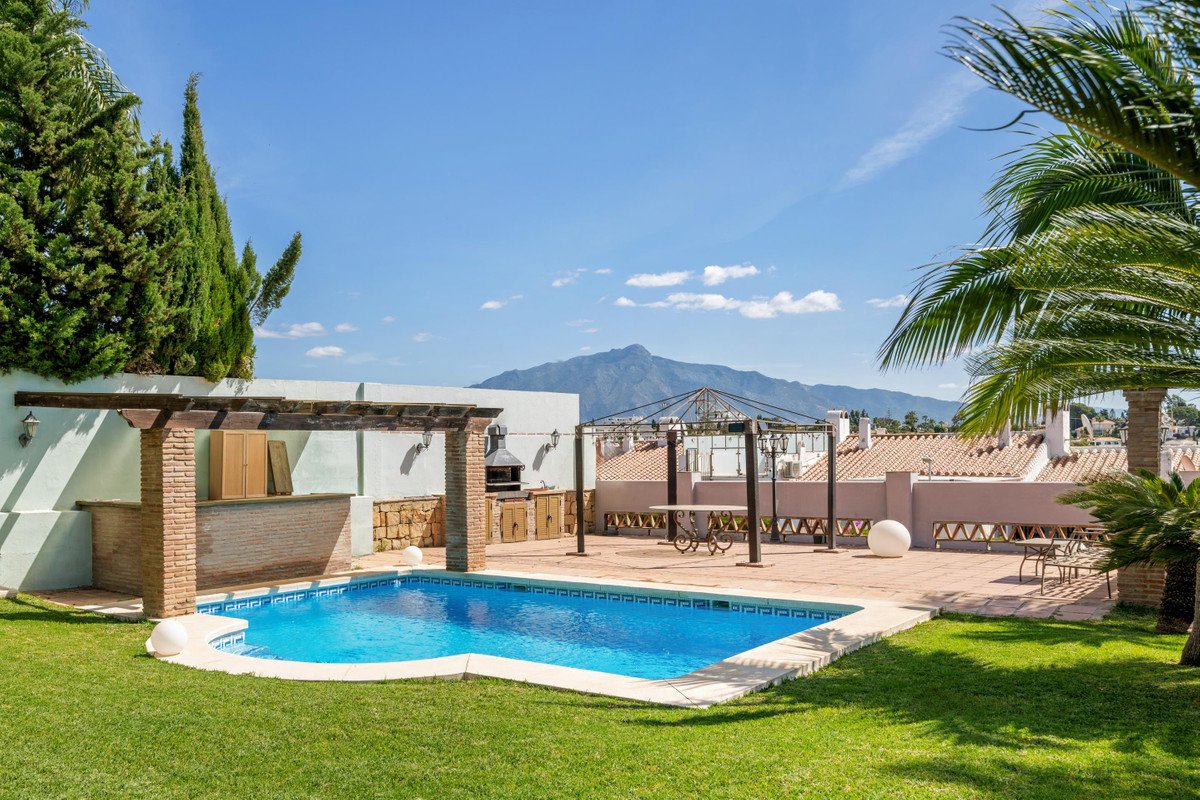 Rooftop terrace with swimming pool, bar area, and distant mountain view under a clear blue sky.