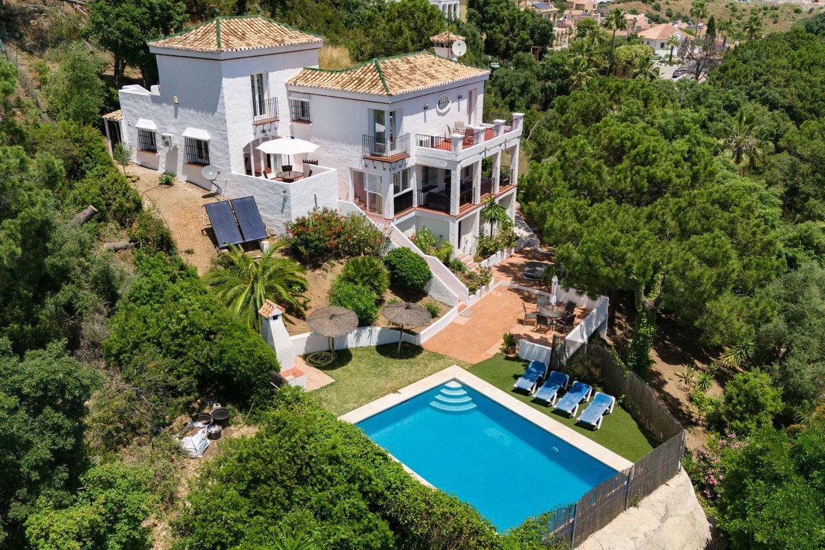 Aerial view of a white villa with tiled roof, private pool, and lush green surroundings.