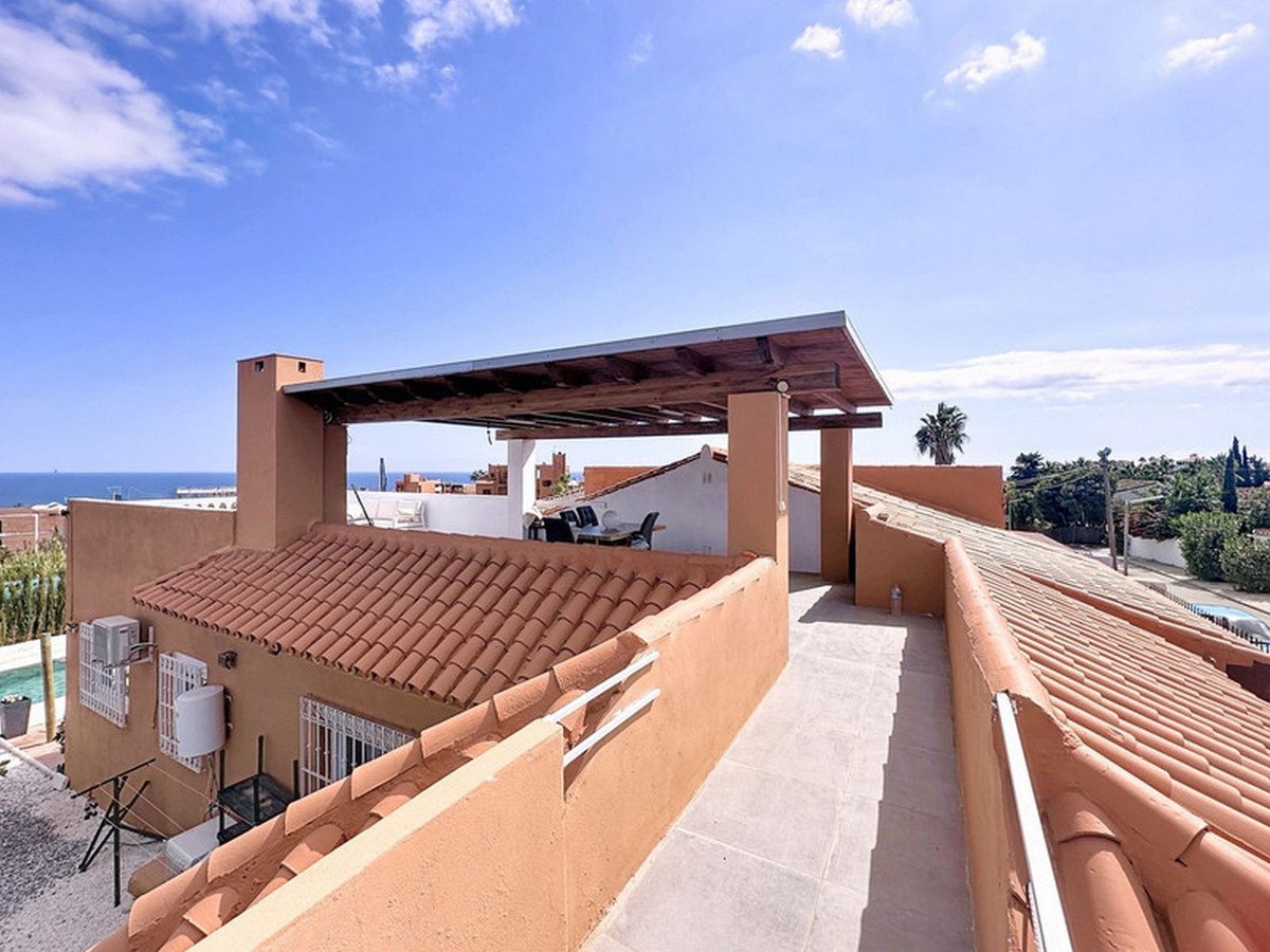 A spacious terrace with a pergola overlooking the sea and surrounding residential area.