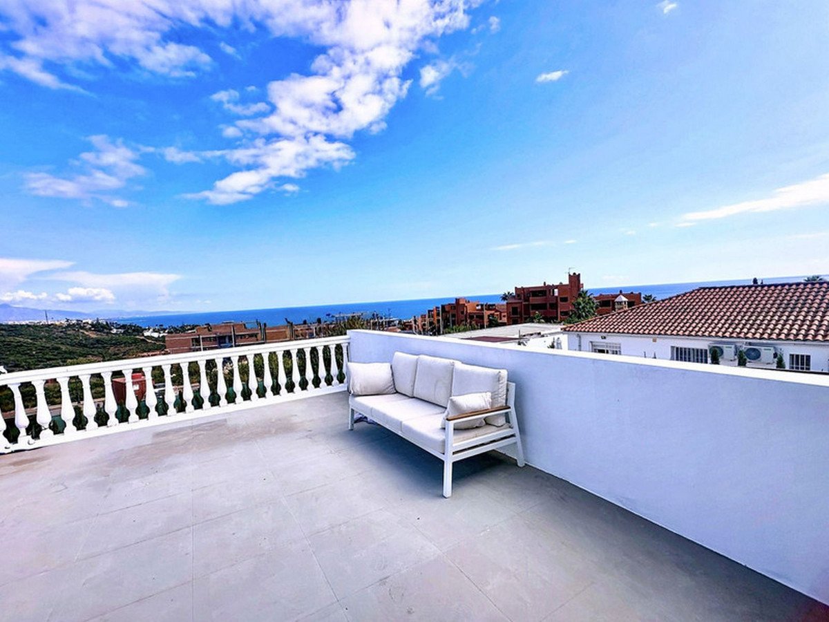 Spacious white terrace with a sofa and a stunning view of the sea and surrounding buildings under a blue sky.