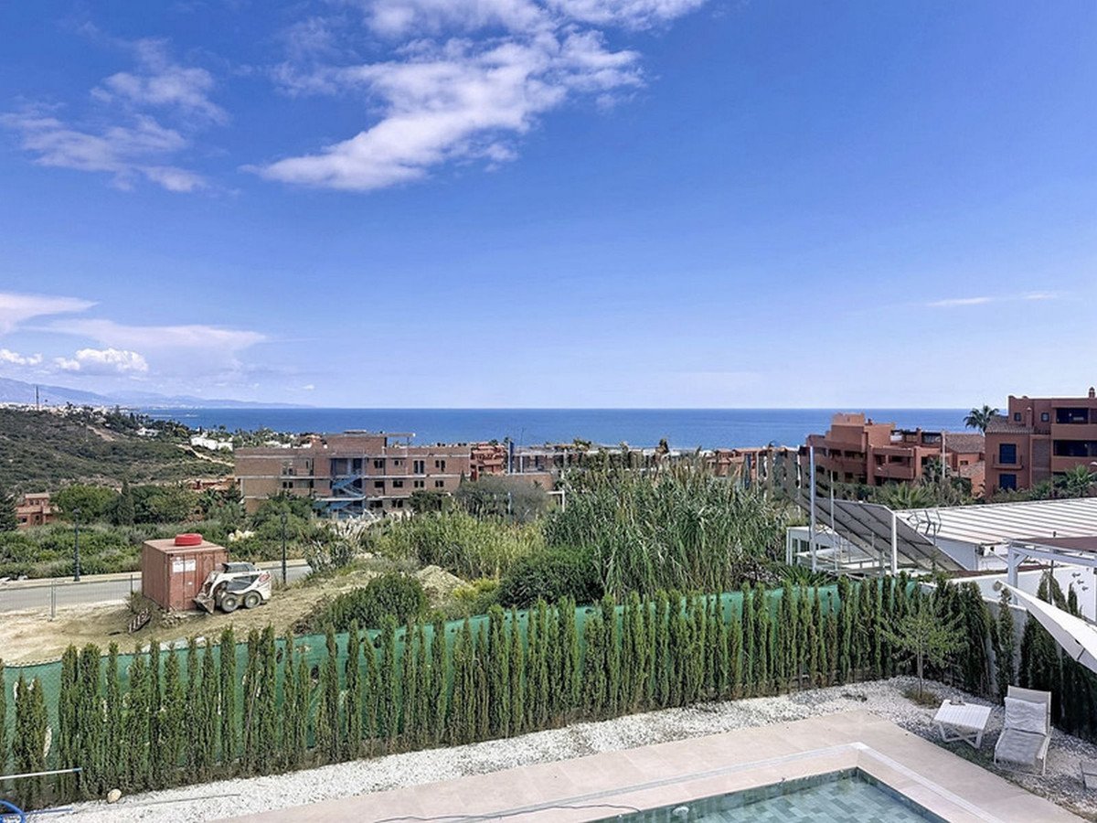 A beautiful sea view from a terrace with a swimming pool and lounge chairs, overlooking distant buildings and hills.