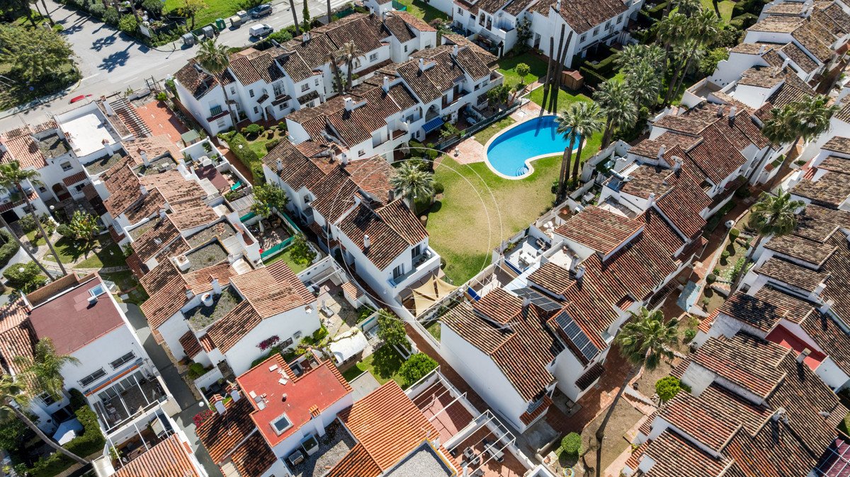 Aerial view of a townhouse complex featuring white buildings with terracotta roofs and a bright blue swimming pool.