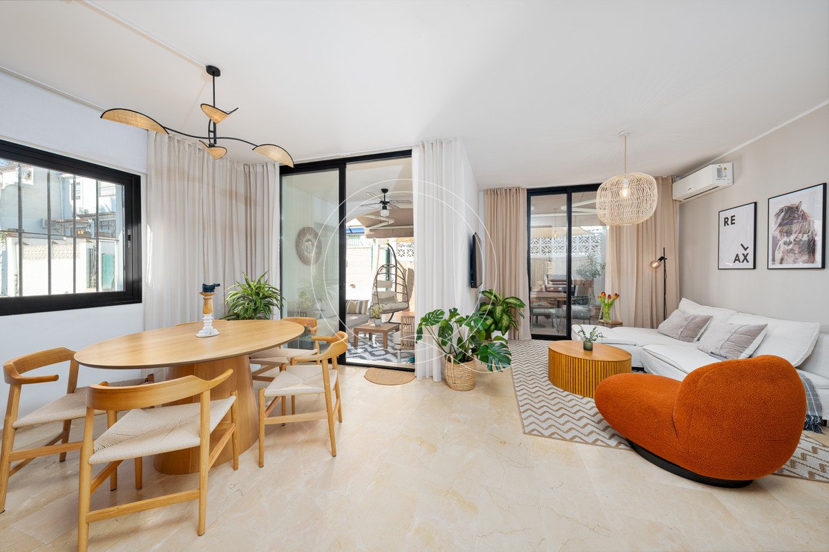 Modern living and dining area with large windows, a comfortable sofa, and a patio view with a hanging chair.