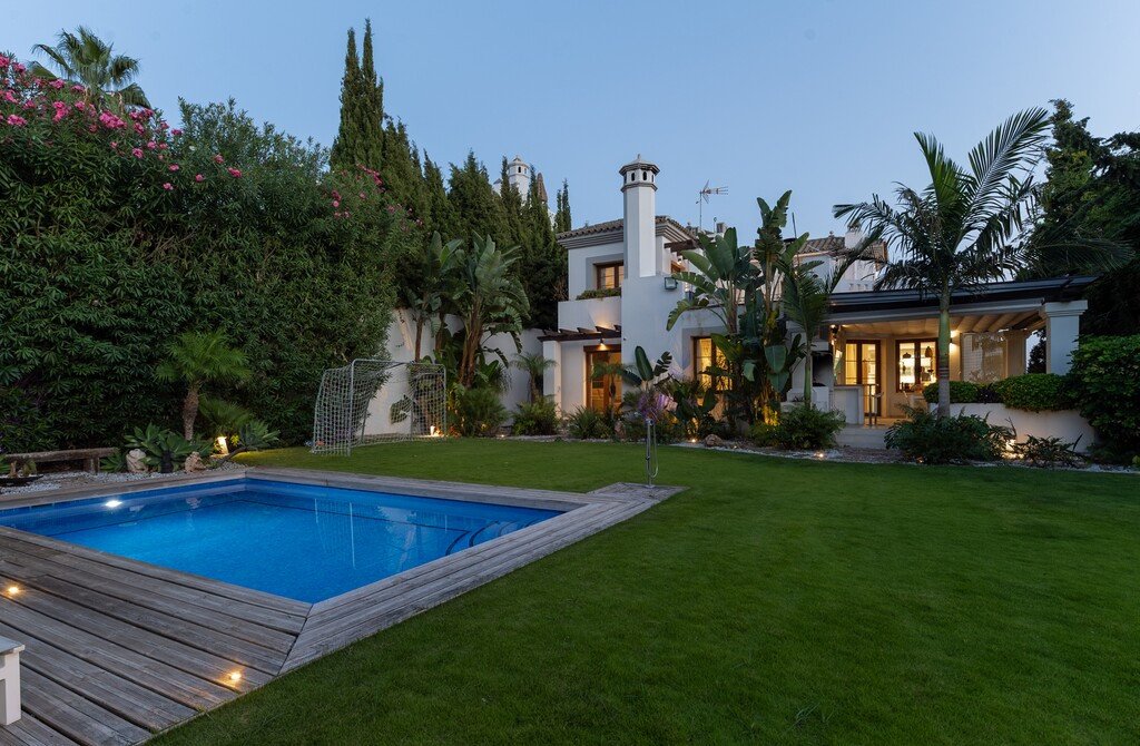 A luxurious villa with a blue swimming pool and a green lawn, featuring a soccer goal and lush garden.