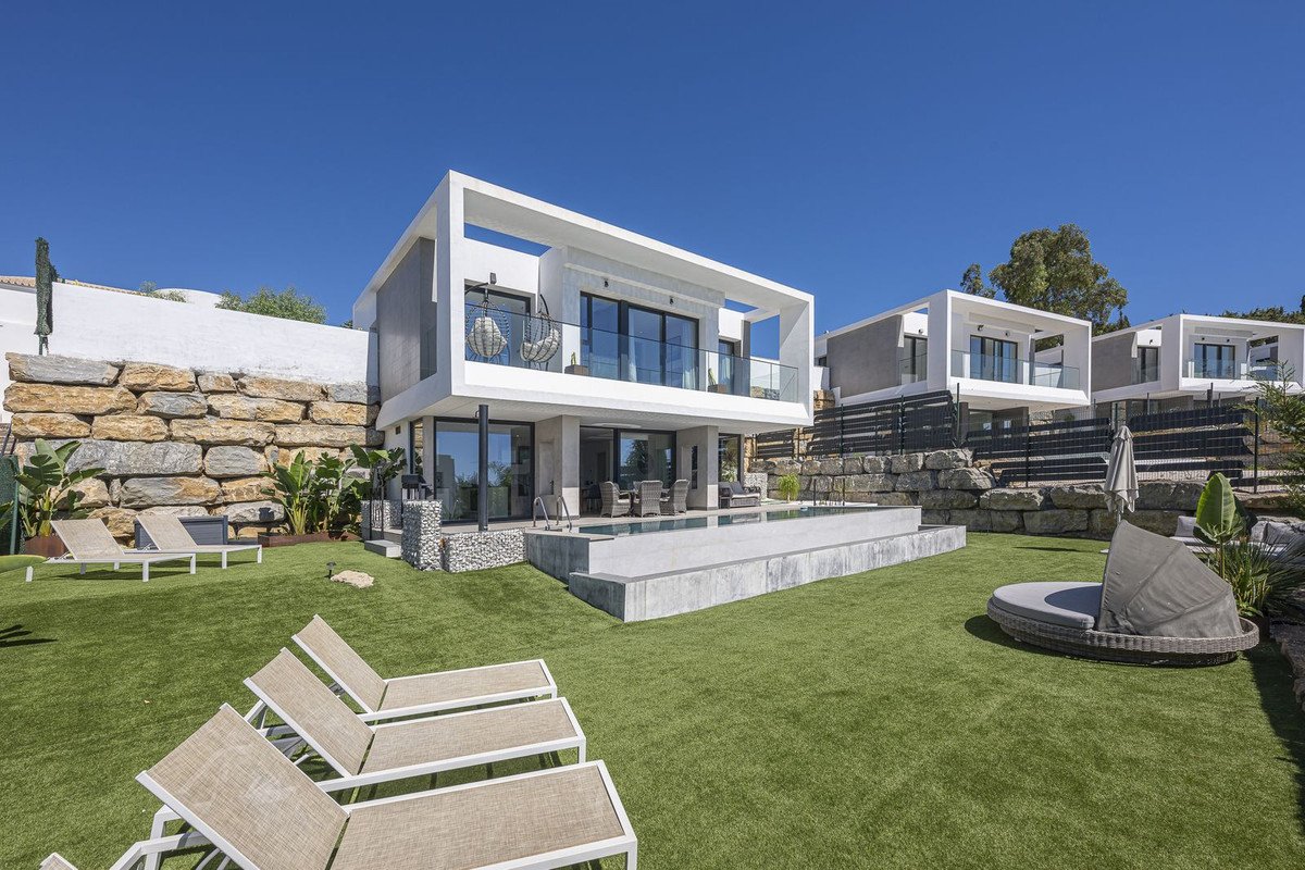 Modern villa with infinity pool, outdoor seating, lounge chairs, and manicured lawn under a clear blue sky.
