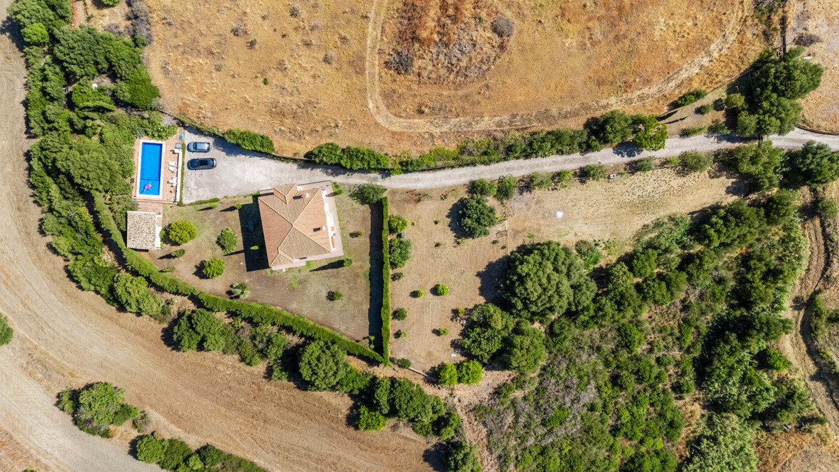 Aerial view of a villa with a pool, surrounded by greenery and dry fields.