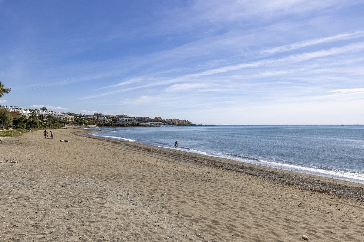 Beachfront property with sandy shore, calm sea, and coastal town view under clear blue sky.