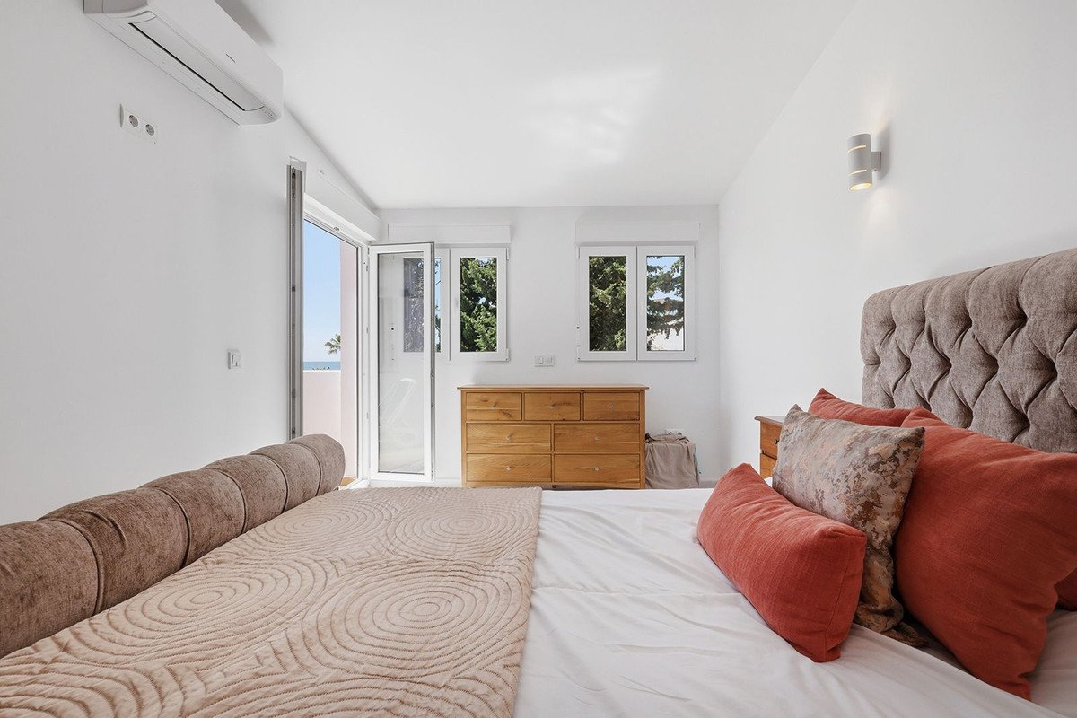 Spacious bedroom with tufted headboard, ocean view through glass doors, wooden dresser, and wall-mounted AC.