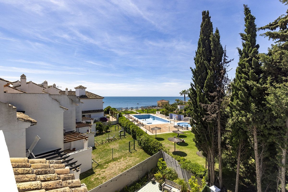 Sea view from a balcony overlooking a pool, green lawn, and white buildings under a blue sky.