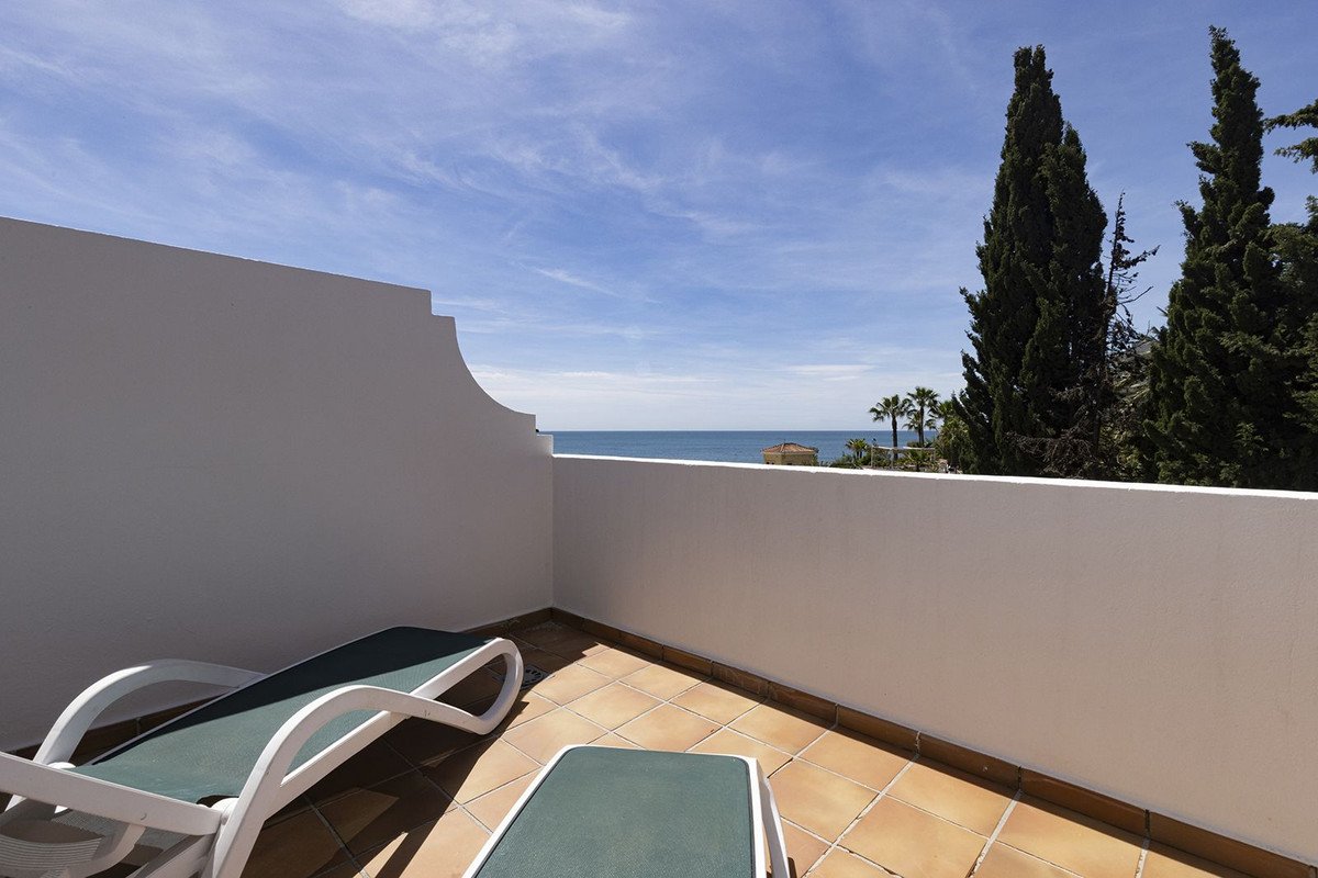 Balcony with lounge chairs, ocean view, and palm trees under a clear blue sky.