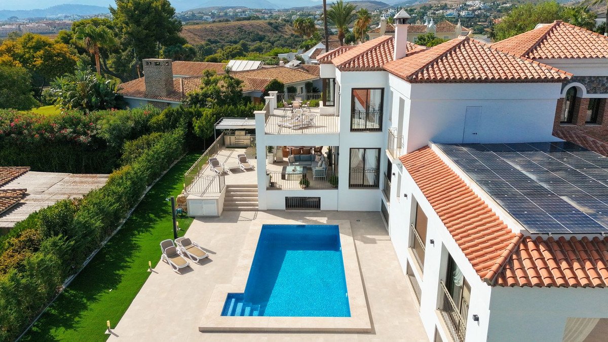 Luxury villa with a private swimming pool, multiple balconies, terraces, and solar panels, surrounded by greenery.