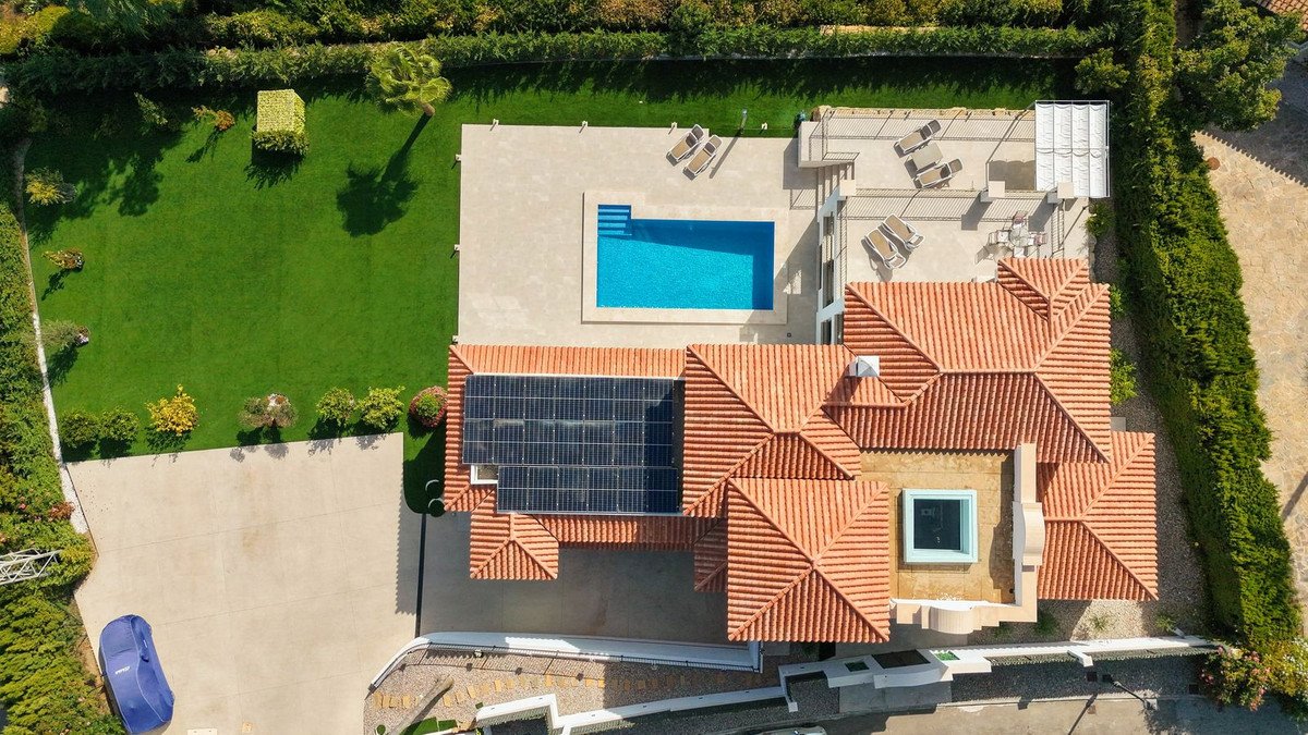 Aerial view of a luxury villa featuring a swimming pool, sun loungers, solar panels on the roof, and a lush green garden.