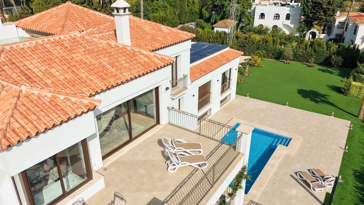 Aerial view of a modern villa with a swimming pool, lounge chairs on the terrace, and a lush green lawn.