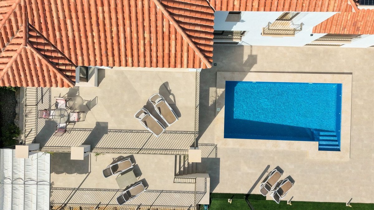 Aerial view of a private villa with a bright blue swimming pool, lounge chairs, and an outdoor dining area.