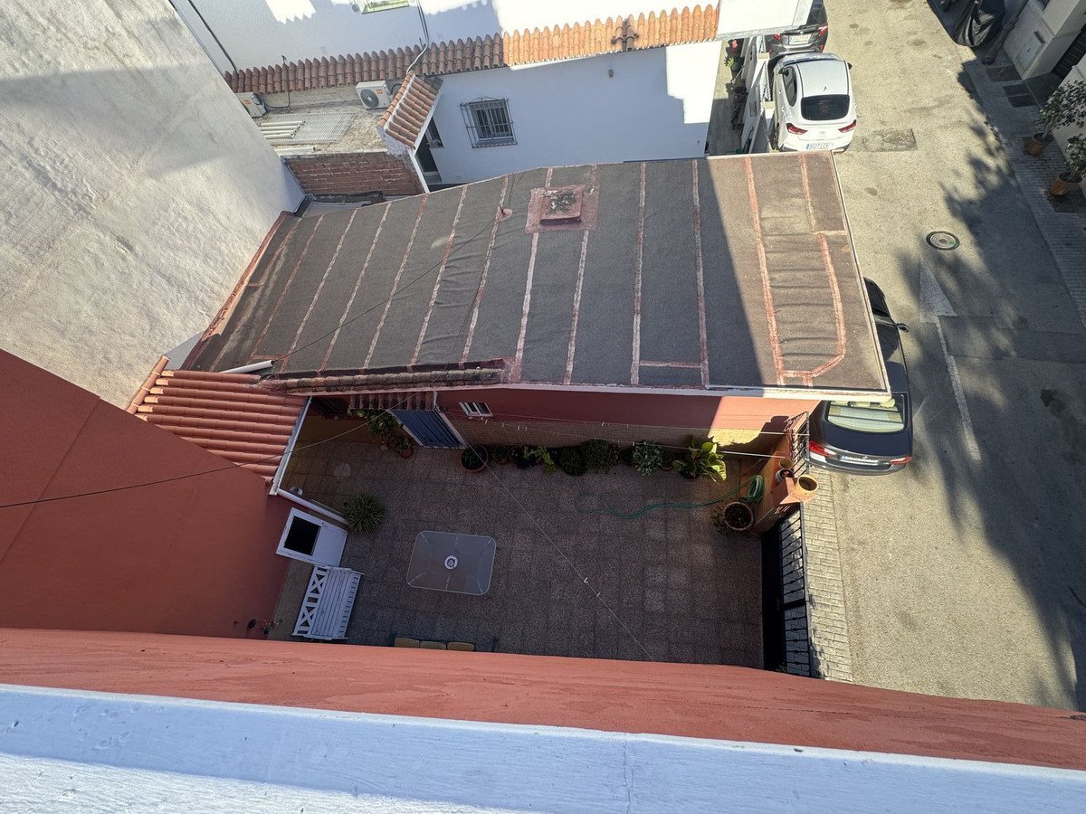 A view from above of a paved terrace with outdoor seating and plants, next to a street with cars.