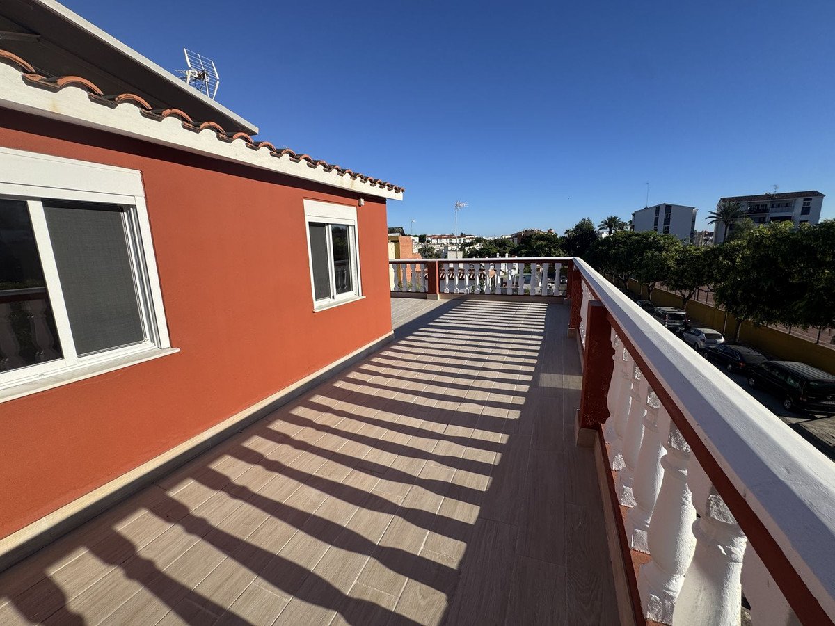 Spacious terrace with decorative railing and tiled floor, offering views of buildings and trees under a clear blue sky.