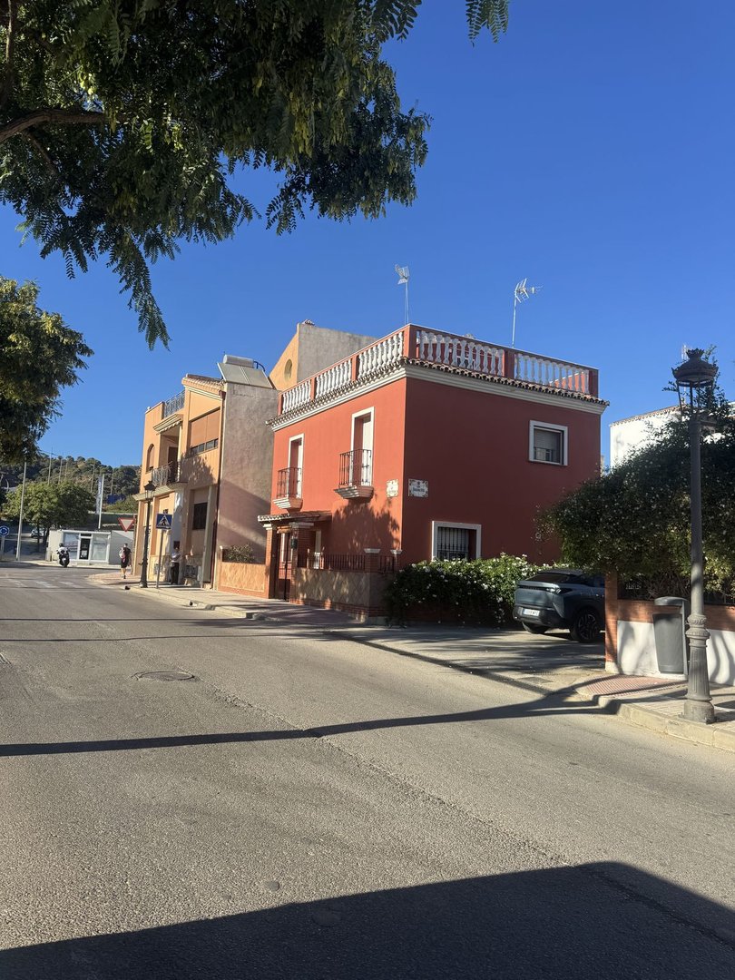 Red terraced house with a balcony and rooftop terrace, next to an orange house, with blue sky.