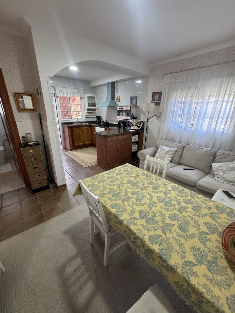 A bright open-plan living area with a dining table, sofa, and a functional kitchen with brick island.