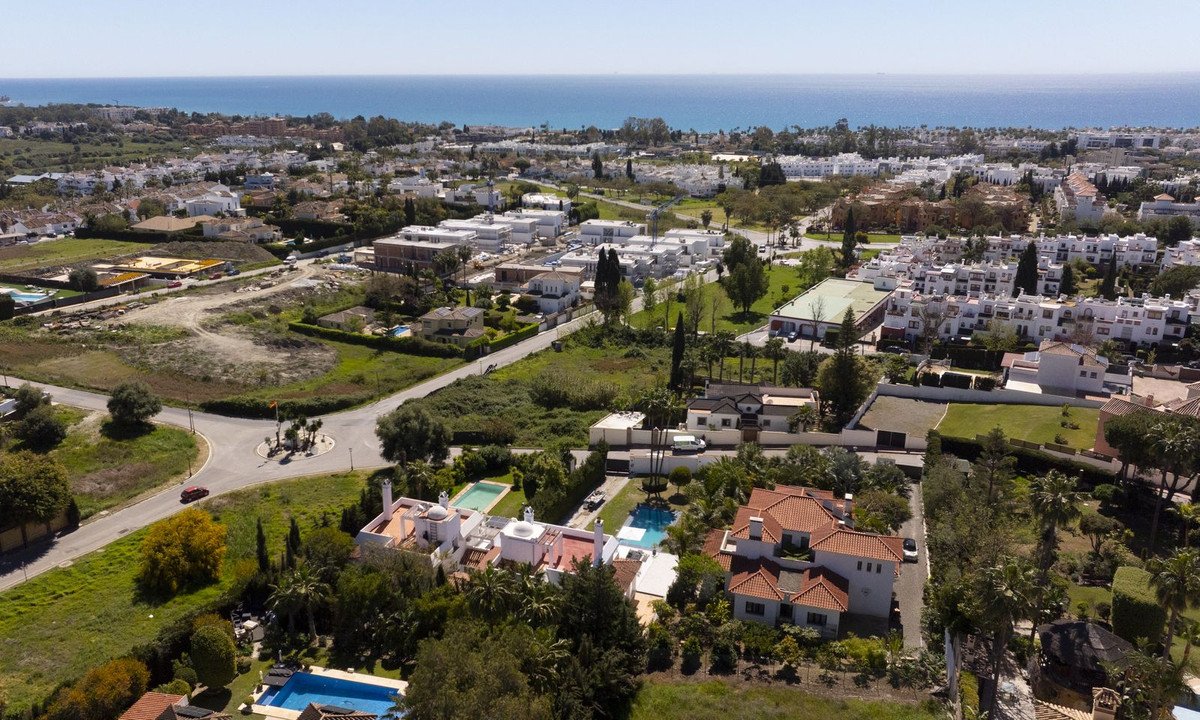 Aerial view of coastal town with villas, pools, and the sea in the background.
