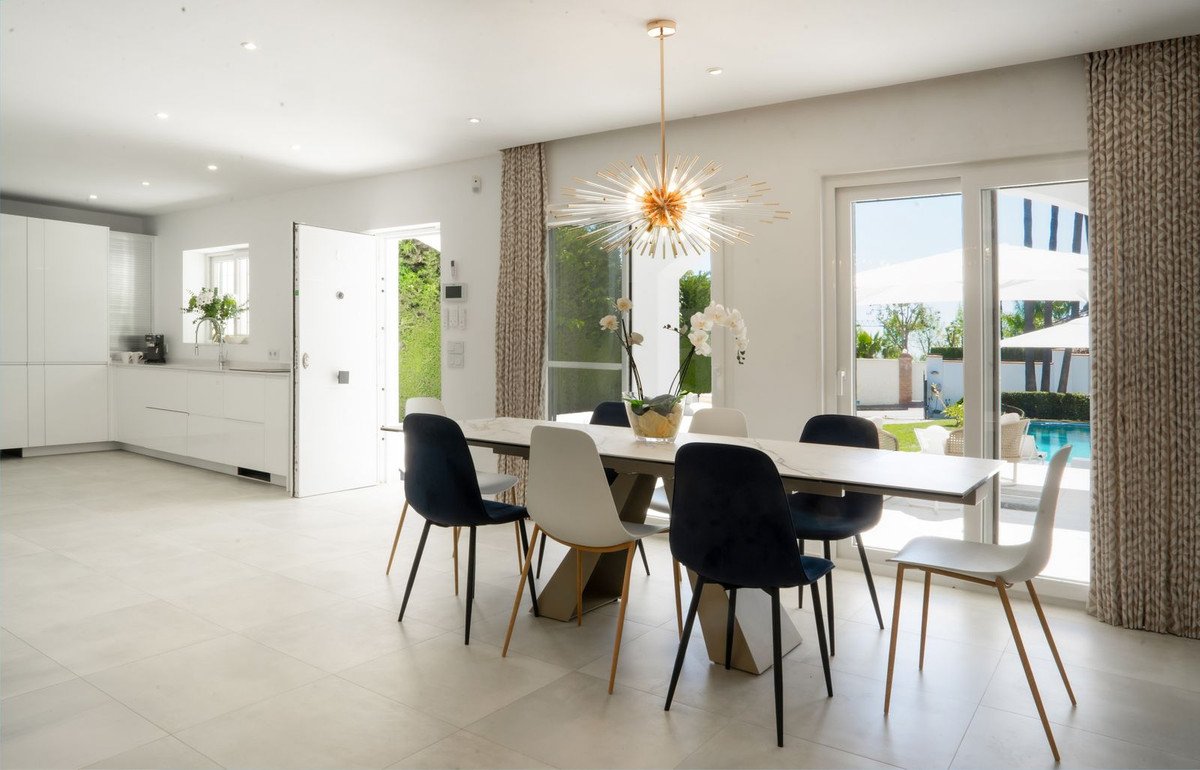 Modern dining room with stylish chairs, a large table, and glass doors opening to a sunny backyard with a swimming pool.