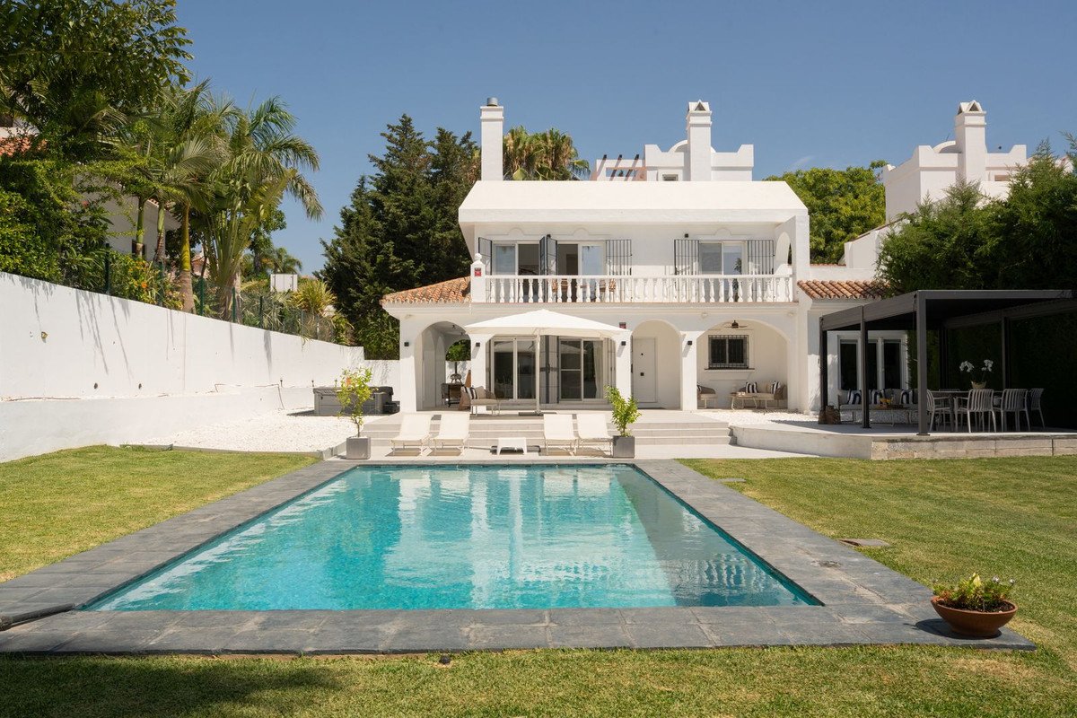A white villa with a swimming pool, loungers, and an outdoor dining area in a sunny garden.