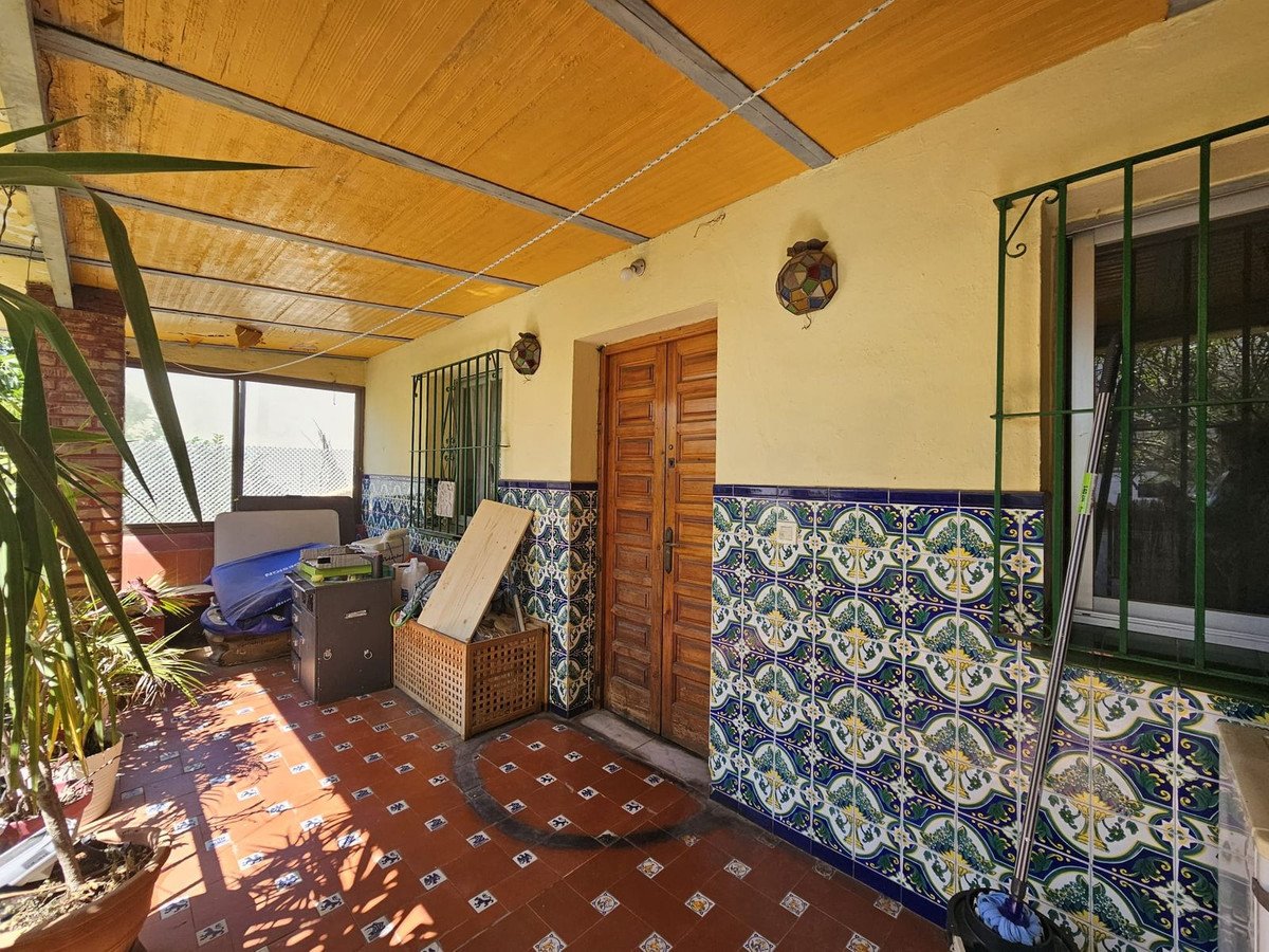 Covered patio with terracotta tiles, colorful tile walls, wooden door, and potted plants.