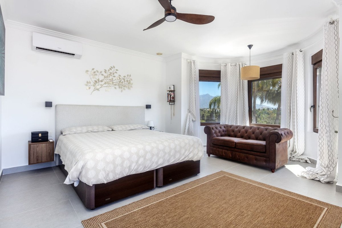 Modern bedroom featuring a large bed, tufted sofa, and scenic ocean view