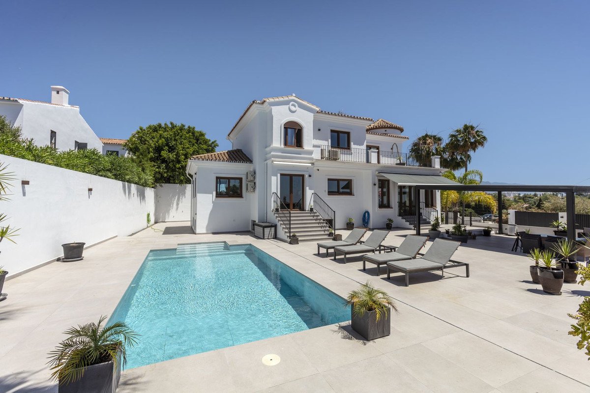 Modern white villa with private pool, sun loungers, and palm trees under clear blue sky.