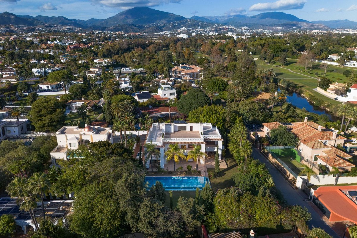 Aerial view of a luxurious home with a swimming pool surrounded by lush greenery and mountains in the background